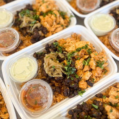 A spicy chipotle chicken bowl with beans, rice and side sauces in a takeout container.