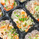 A traditional sesame chicken plate with spring vegetables served over a bed of noodles.