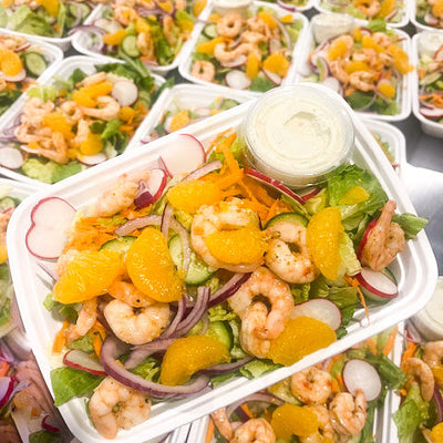 An Asian style shrimp and mandarin salad topped with red onions, carrots and radish with dressing on the side.